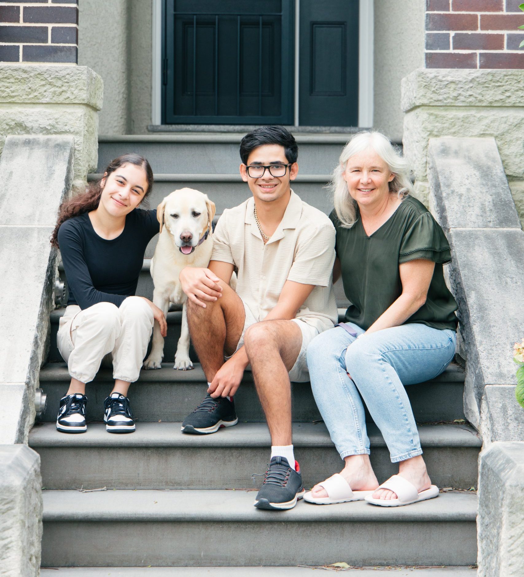 A family of 3 sitting on some steps with their dog
